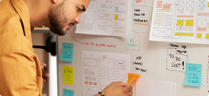 Profissional organizando fluxos de processo em um quadro com wireframes e notas adesivas