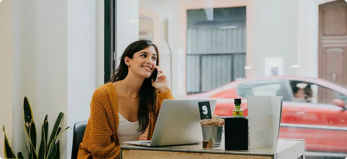 Criadora de conteúdo trabalhando no notebook enquanto fala ao celular