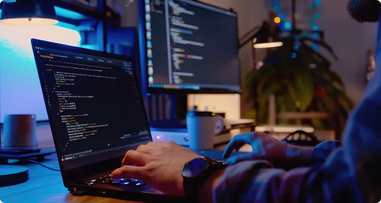 Desenvolvedor programando um site no notebook, com o código também aberto em um segundo monitor