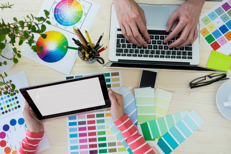 Mãos apoiadas em notebook e várias paletas de cores de design gráfico espalhadas