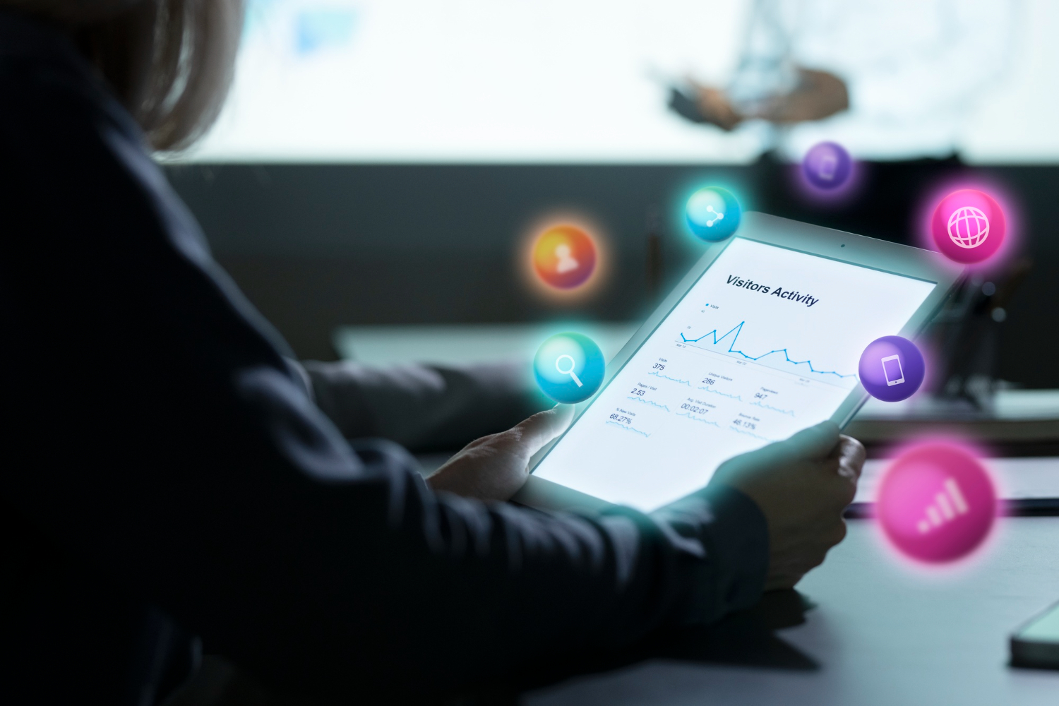 Pessoa analisando gráficos de métricas de desempenho digital em um tablet, com ícones flutuantes representando redes sociais, busca, conexão e dispositivos móveis, simbolizando estratégias de marketing digital e presença online.